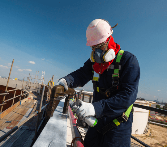 an expert electrician giving the final touch in the roof top by spry the pipe with the full safety mask, gloves and helmet.