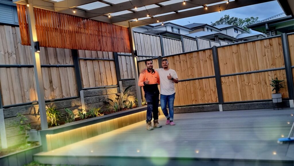 Two men posing for a photo after completion of fitting and lightning the newly built wooden fence.