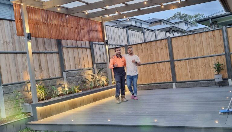 Two men posing for a photo after completion of fitting and lightning the newly built wooden fence.